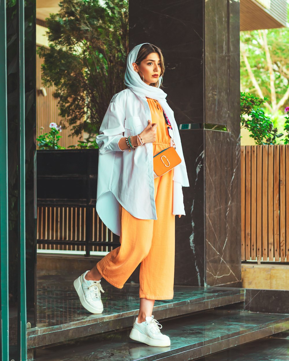 Woman wearing a pale blue oversized shirt, mustard wide-leg trousers and white sneakers outdoors
