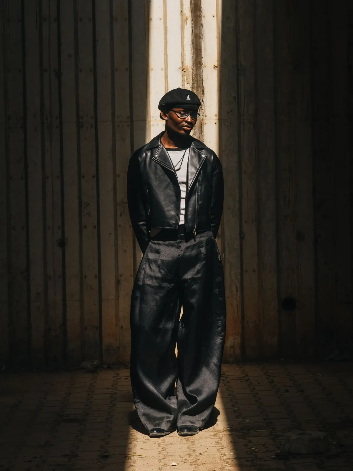 A person in wide-leg trousers and a leather jacket standing in sunlight.