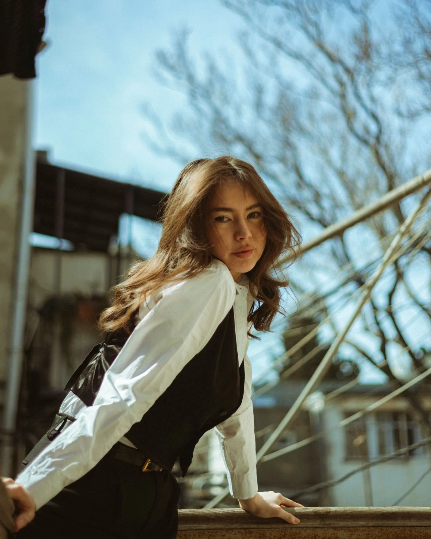 A woman in a dark waistcoat over a pale blouse beside outdoor stairs.