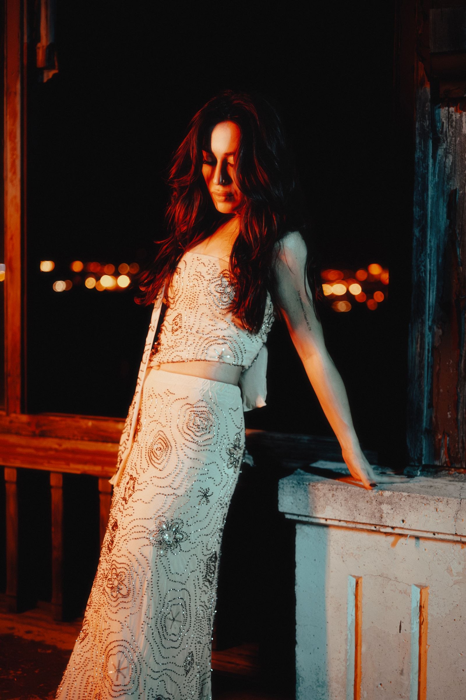 A woman in a pale patterned dress beside a balcony at night.