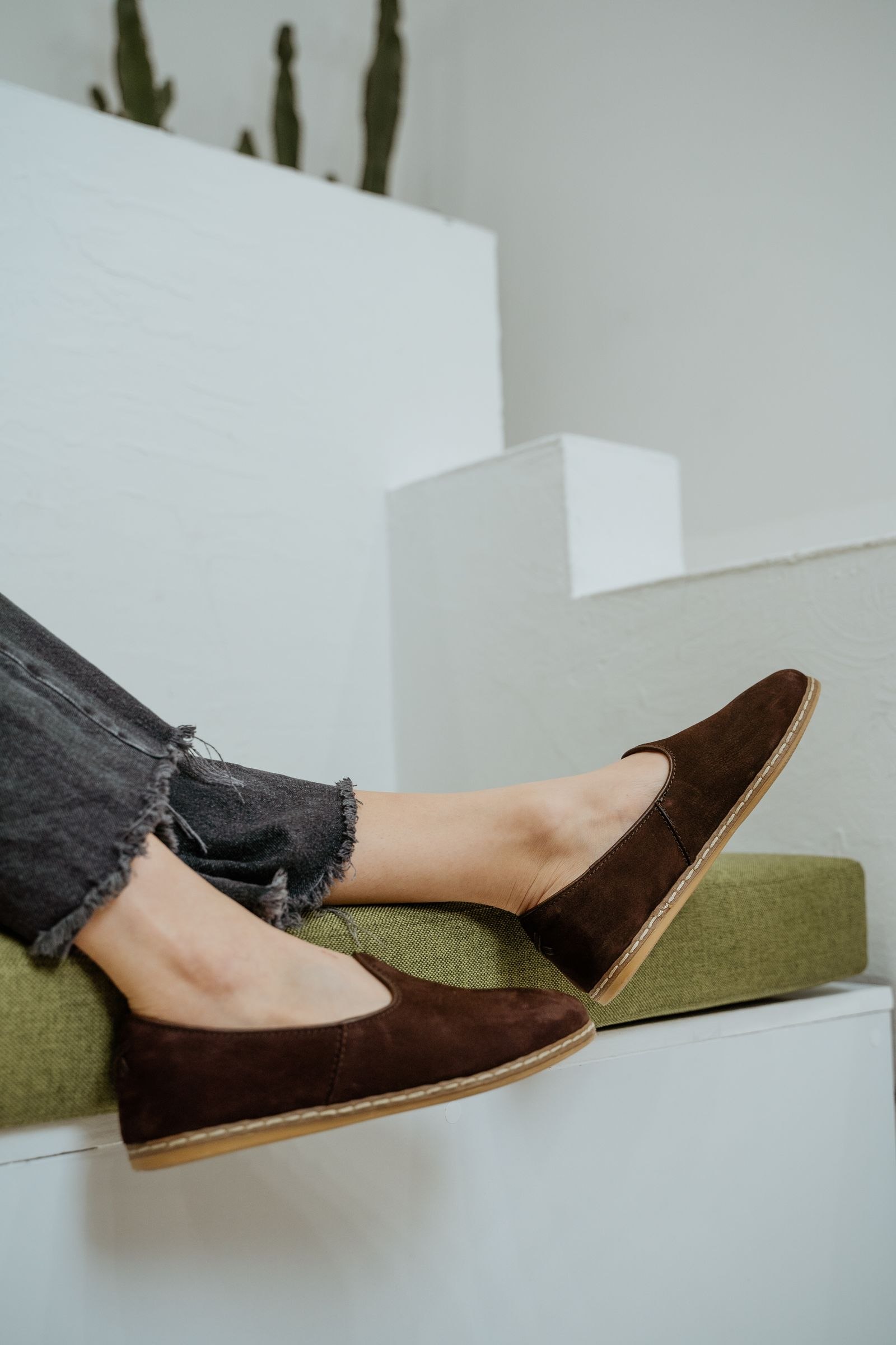 Brown slip-on shoes beneath dark jeans with frayed hems.