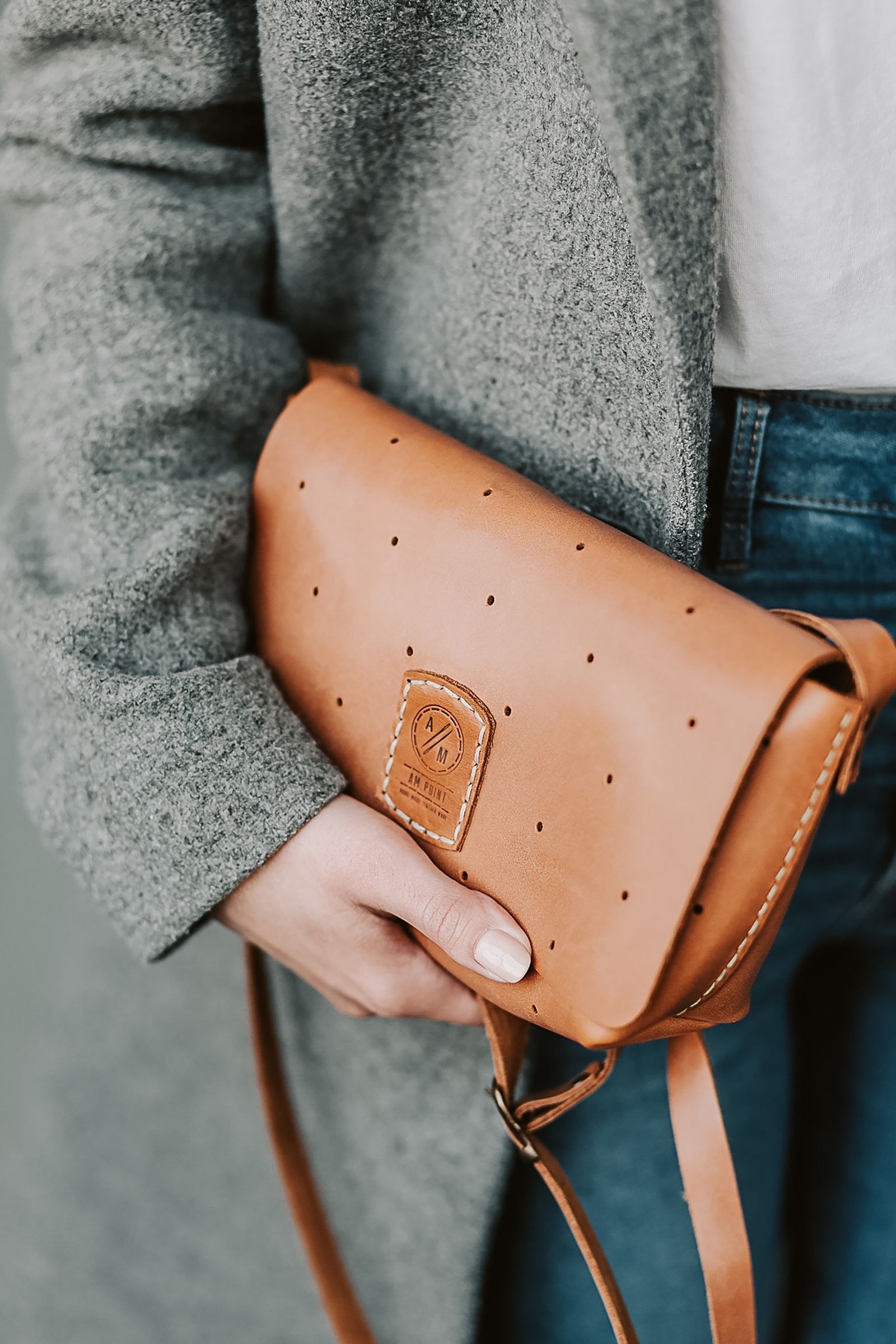 A tan shoulder bag held beside a grey coat and jeans.