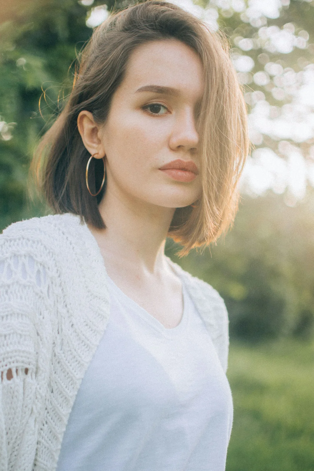 A woman in a pale top and open-textured pale cardigan outdoors.