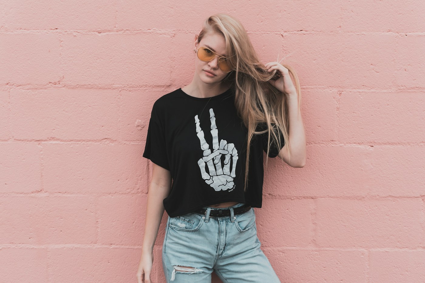 A woman in a black T-shirt and light denim shorts beside a pink wall.