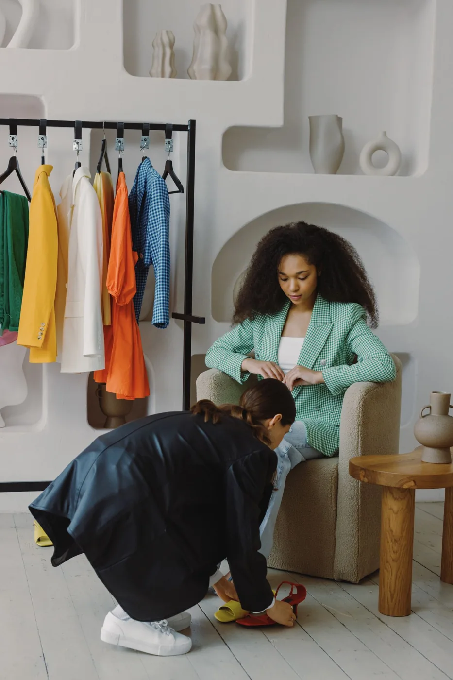 Two women examining footwear in a room with clothes and shoes.