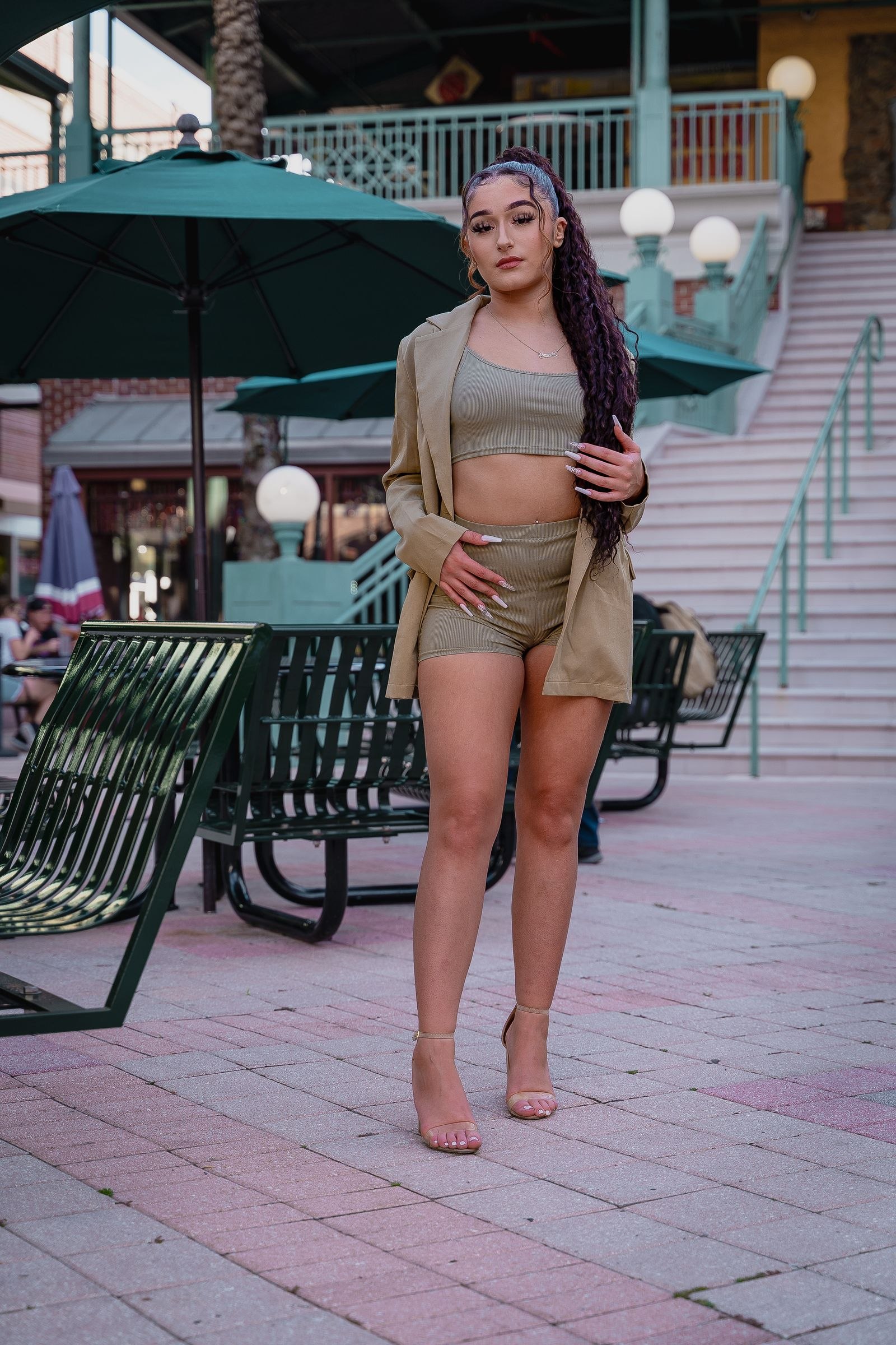 A woman wearing a pale jacket and shorts on a paved street.