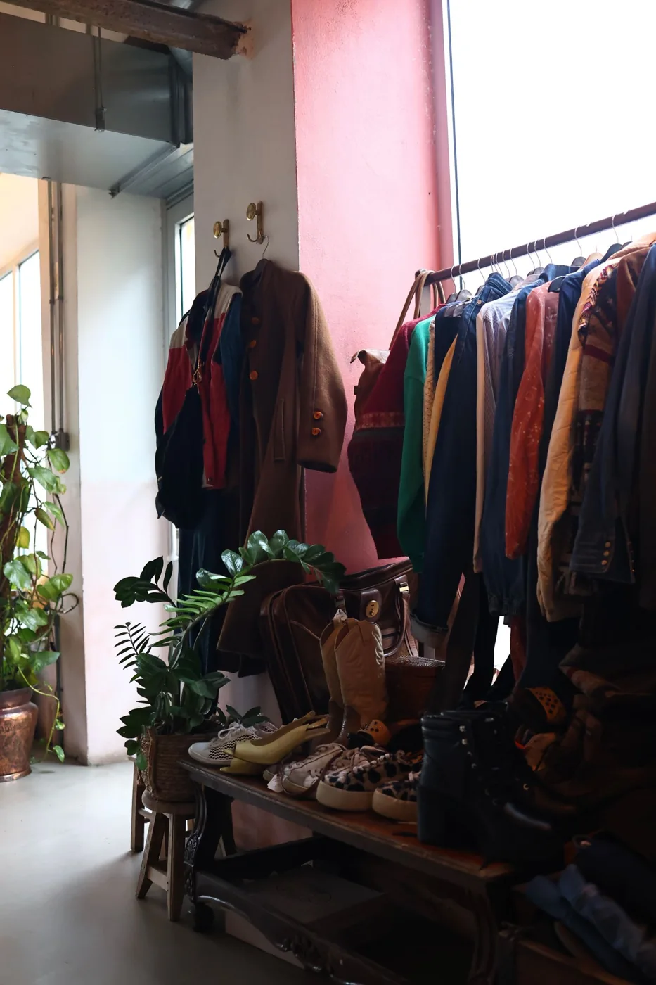 Coats and other garments on a rail beside a bright shop window.