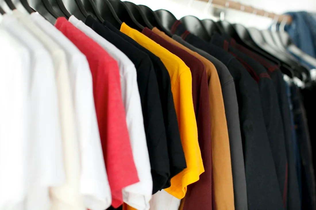 Pale, red, yellow and dark shirts grouped on hangers along a rail.