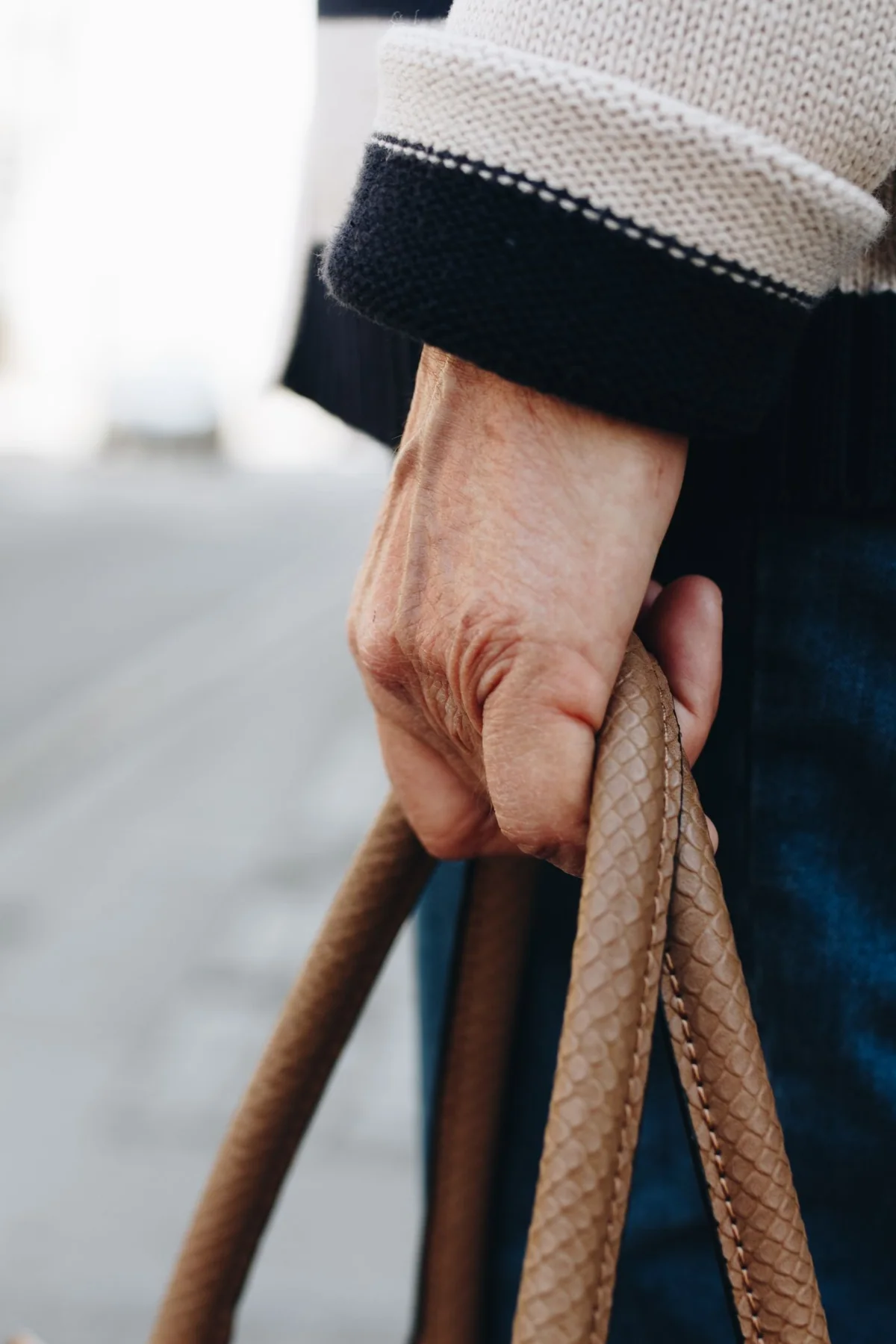 A close view of a hand holding the handles of a textured brown bag.