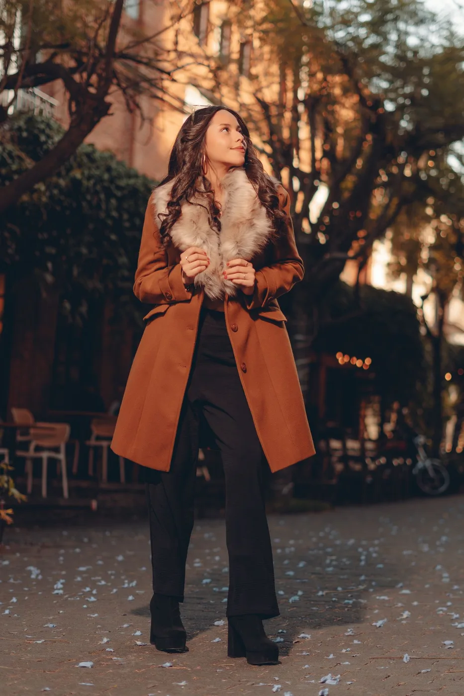 A woman wearing a brown outer layer among autumn trees.