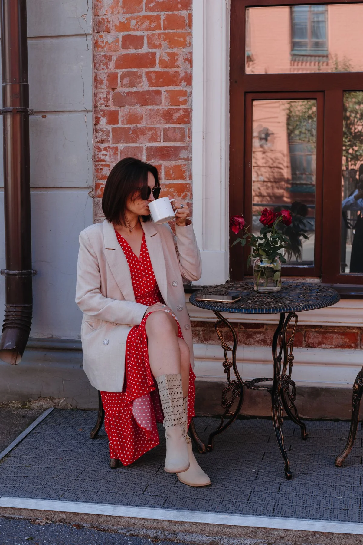 A woman in a red outfit and a pale outer layer beside an outdoor cafe table.