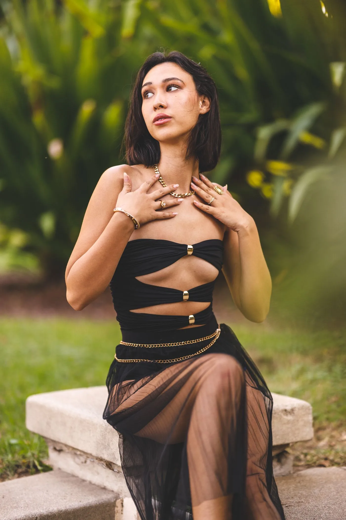 A woman in a dark cut-out dress among green plants.