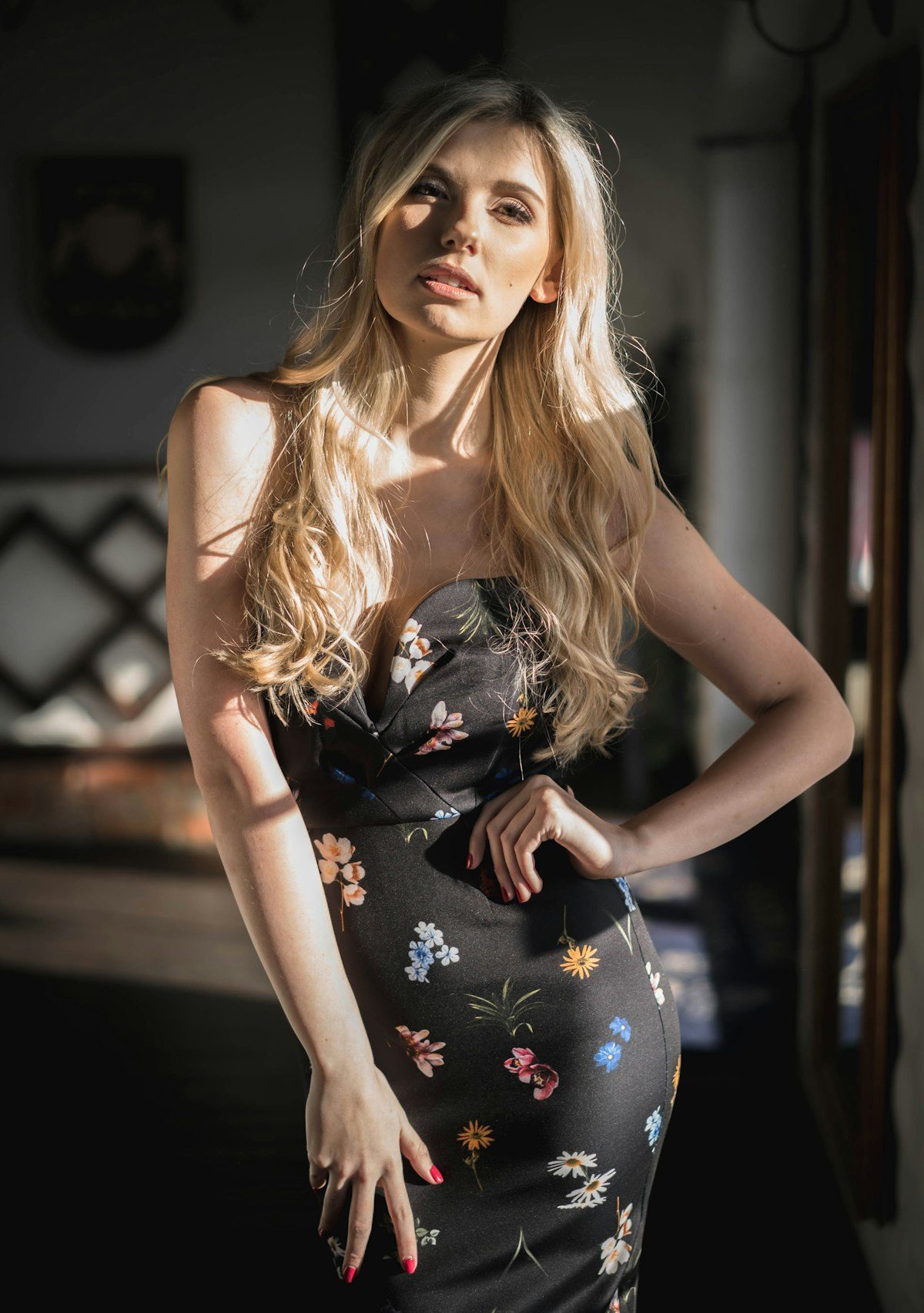 A woman in a dark floral dress beside a window.