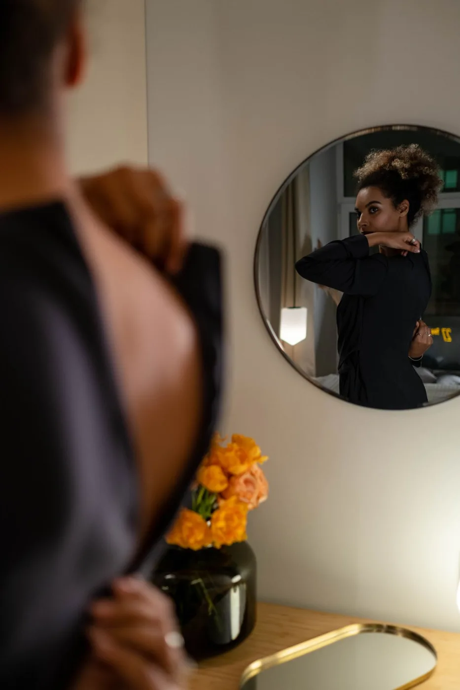 A person in a dark garment beside a round wall mirror.