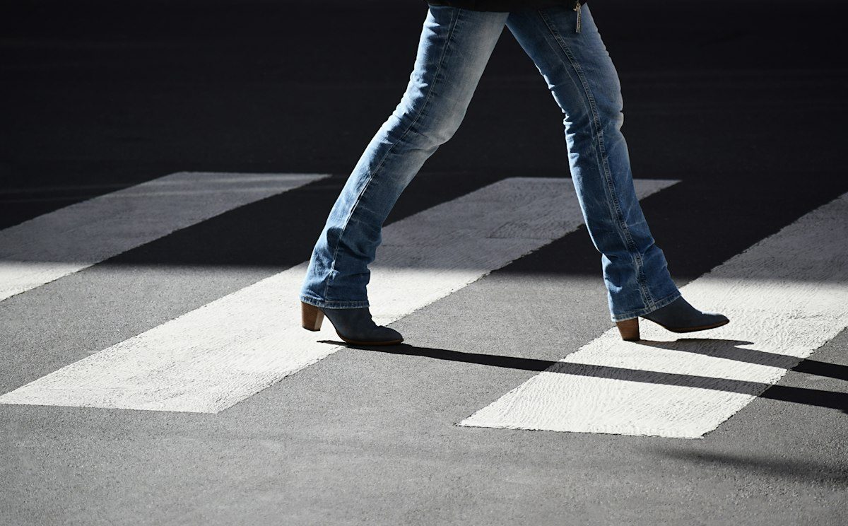 A person in blue jeans walking across a marked pedestrian crossing.