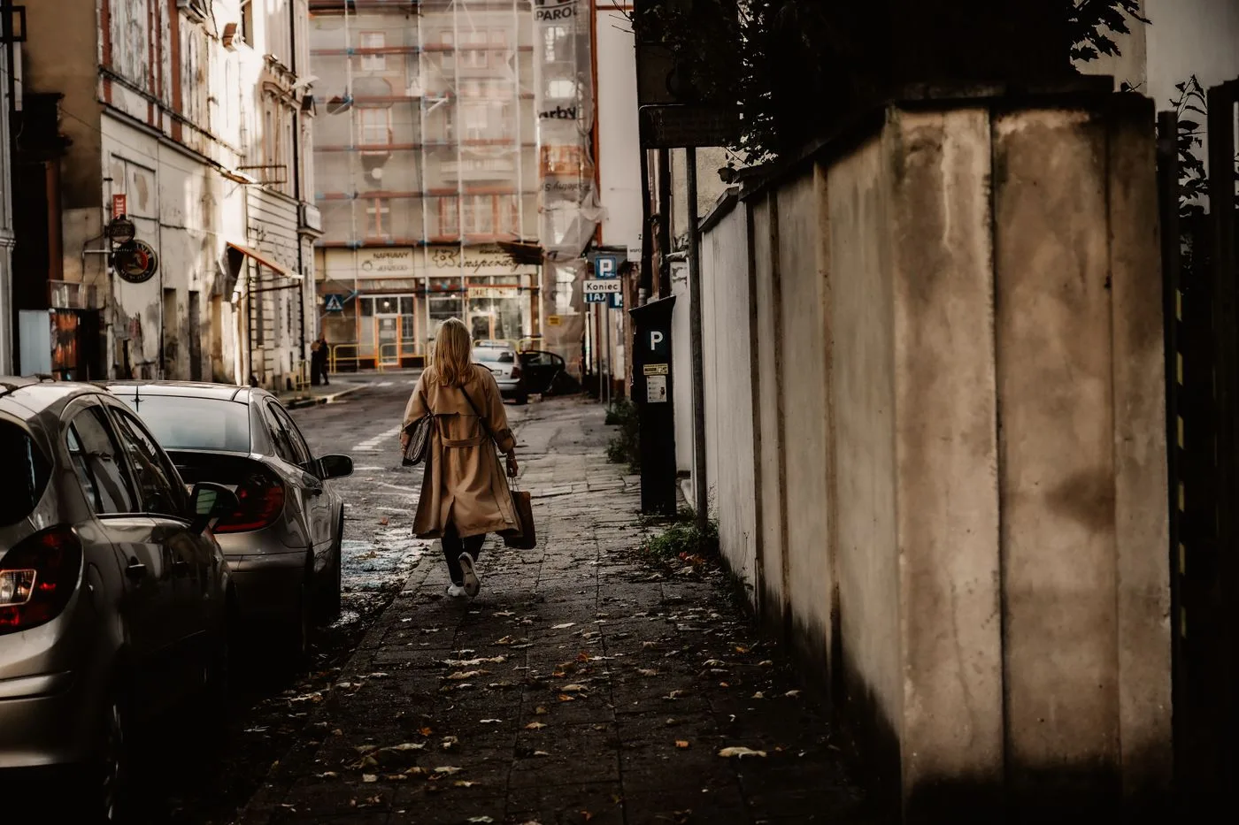 A woman in a long outer layer on a narrow city street.