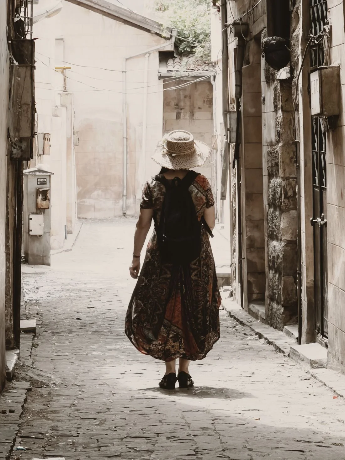 A woman in a long floral dress on a narrow stone street.