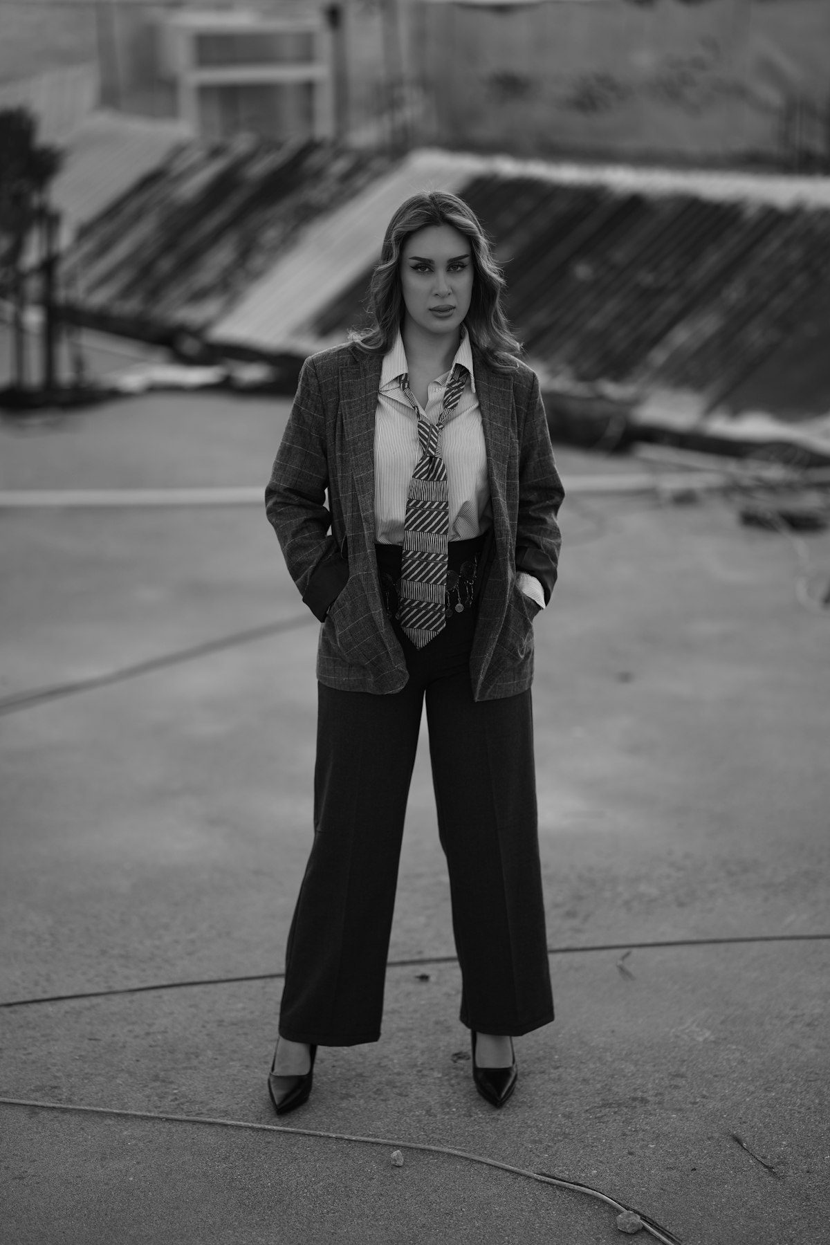 A monochrome photograph of a woman in a jacket and wide-leg trousers outdoors.