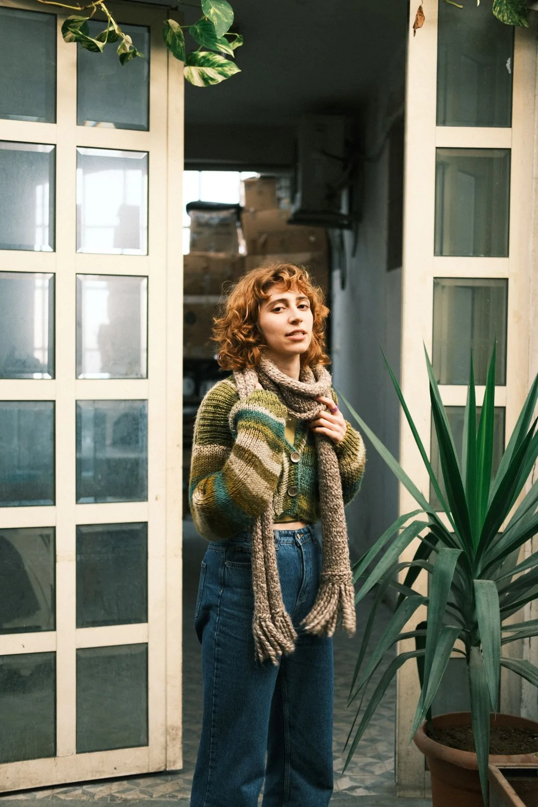 A woman wearing a scarf and knit top beside a glazed doorway.