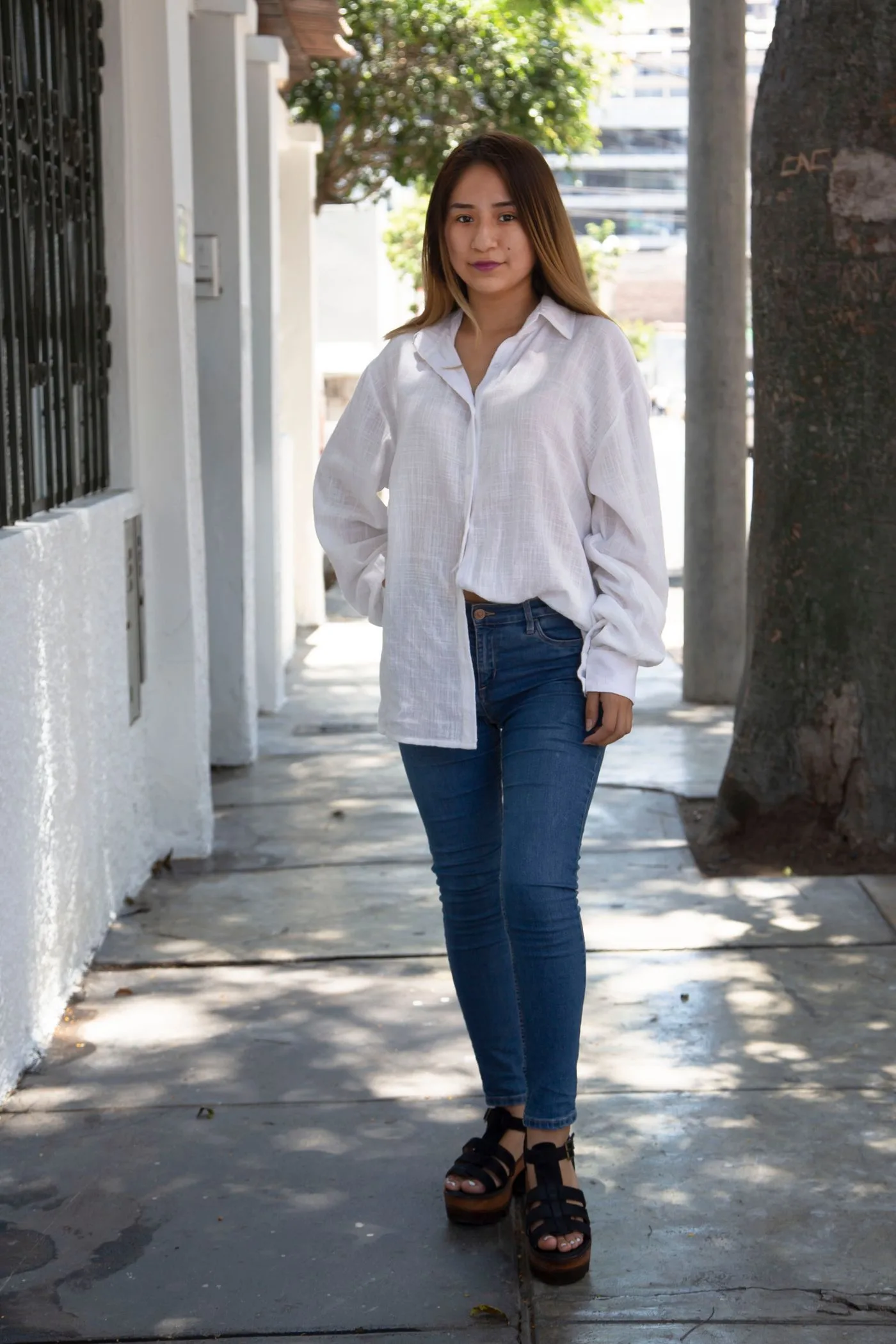 A woman wearing a pale shirt and jeans on a city pavement.