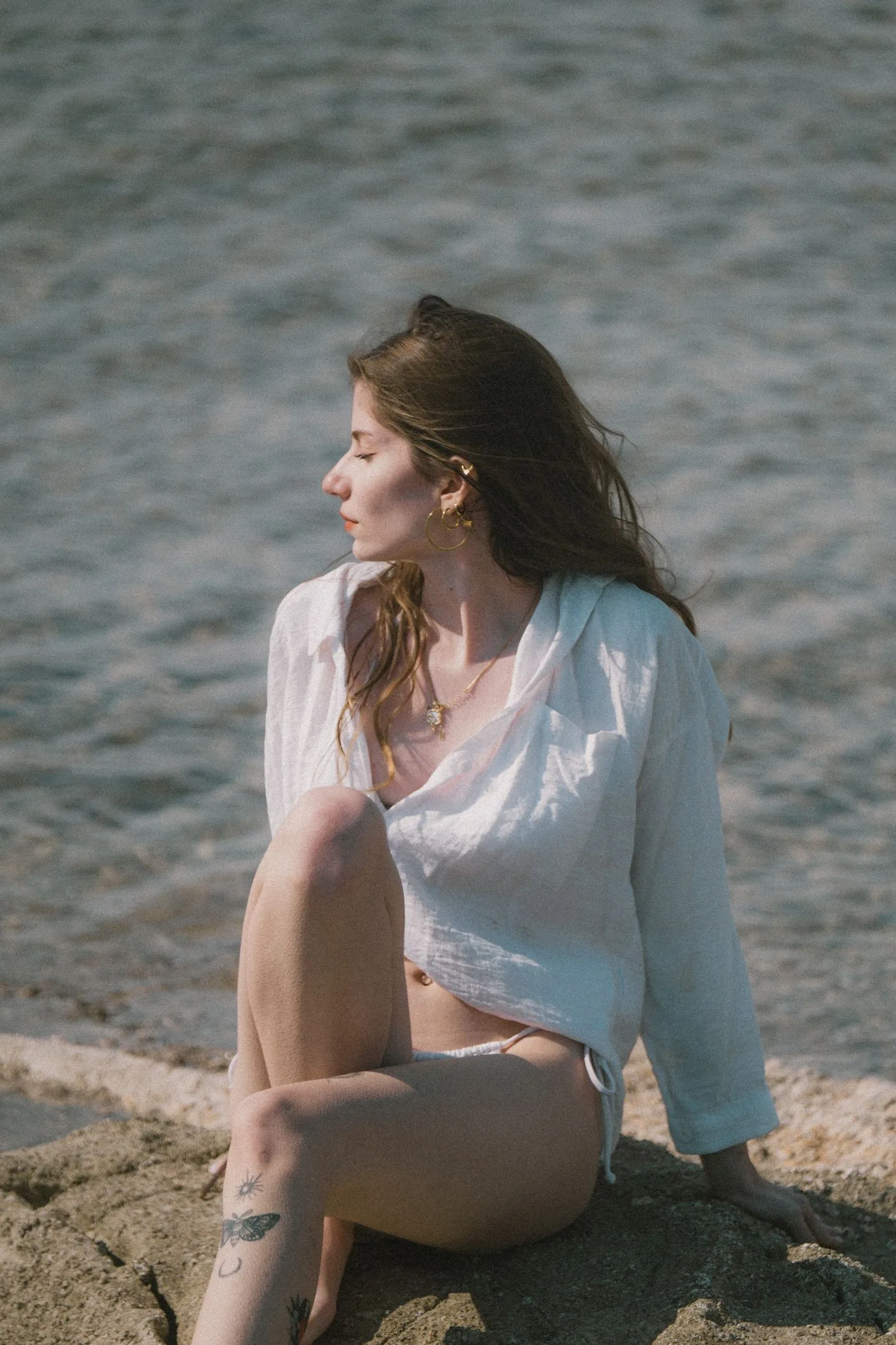 A woman in a pale collared shirt seated beside the sea.