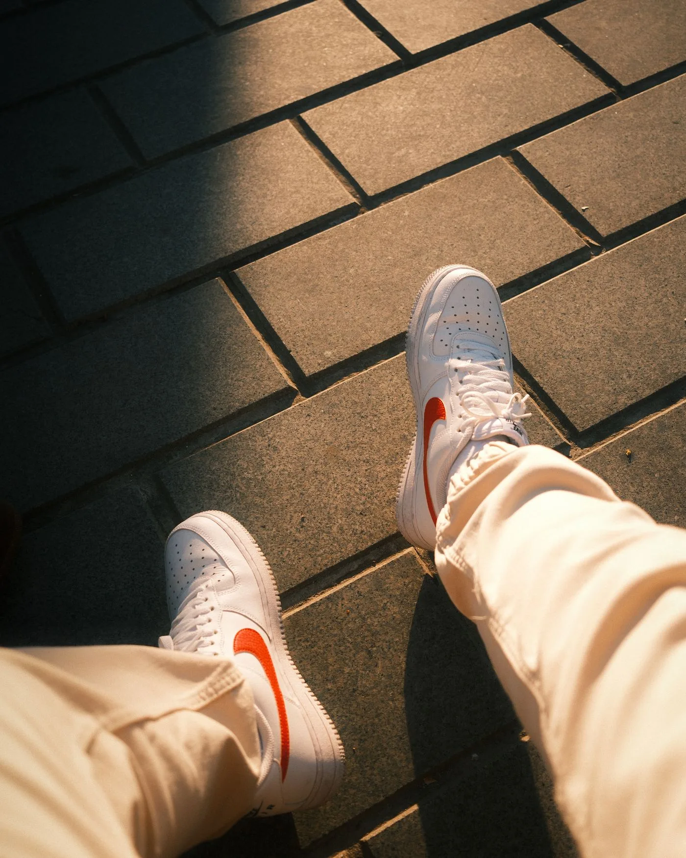 Pale sneakers and light trousers above a paved surface.