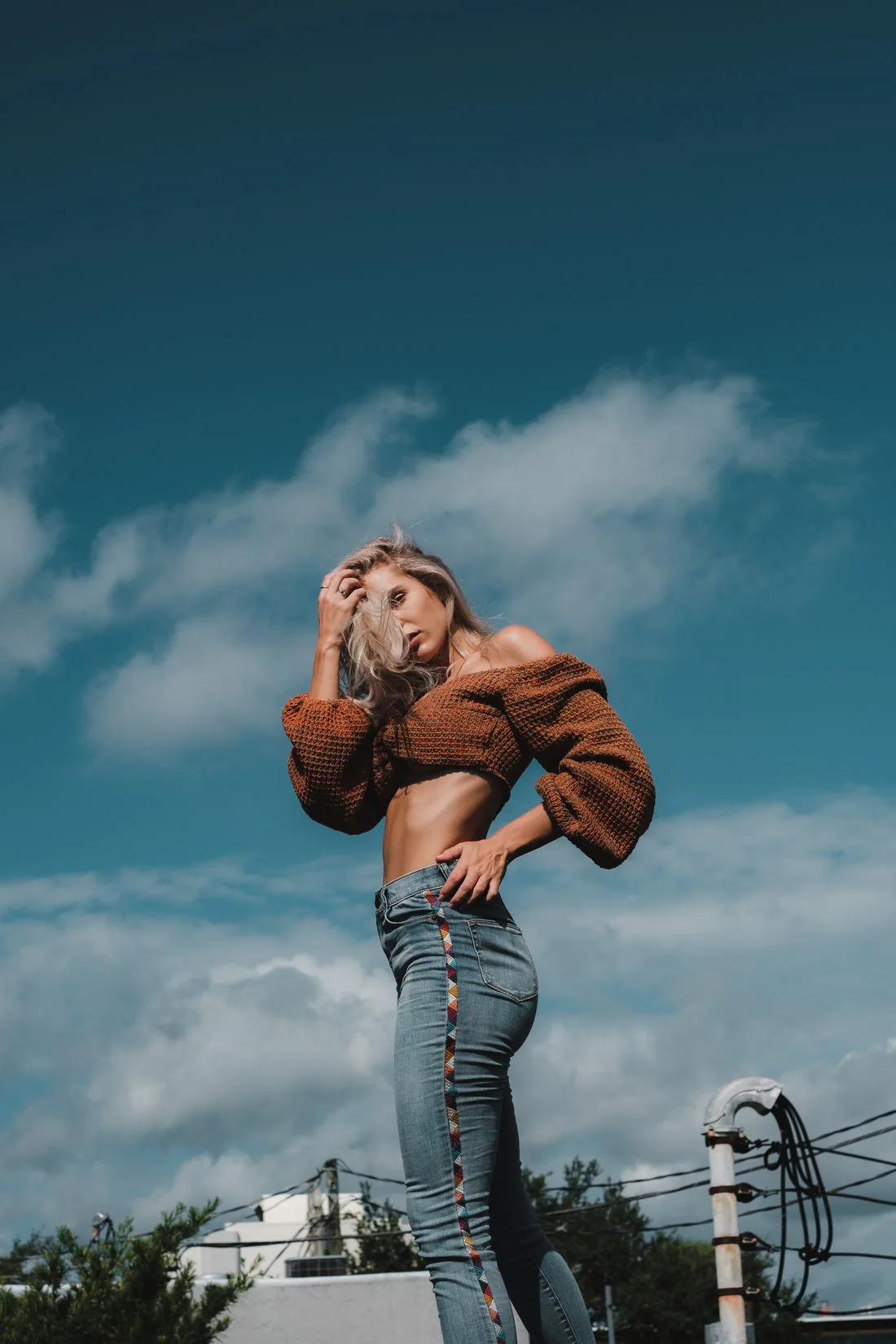A woman in a brown sweater and jeans beneath a blue sky.