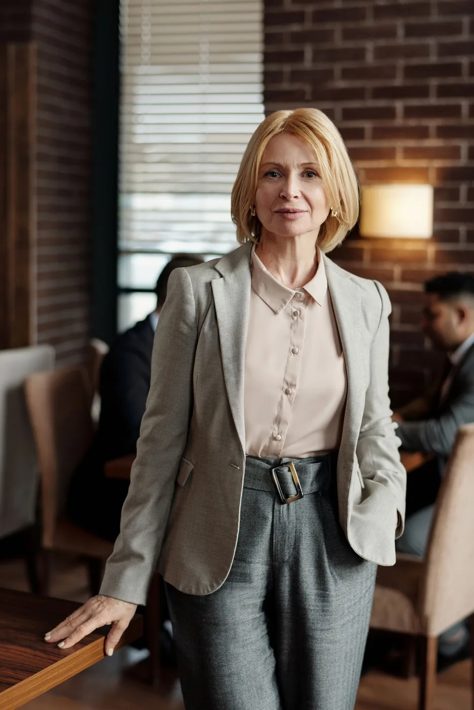 A woman wearing a pale jacket over a light blouse indoors.