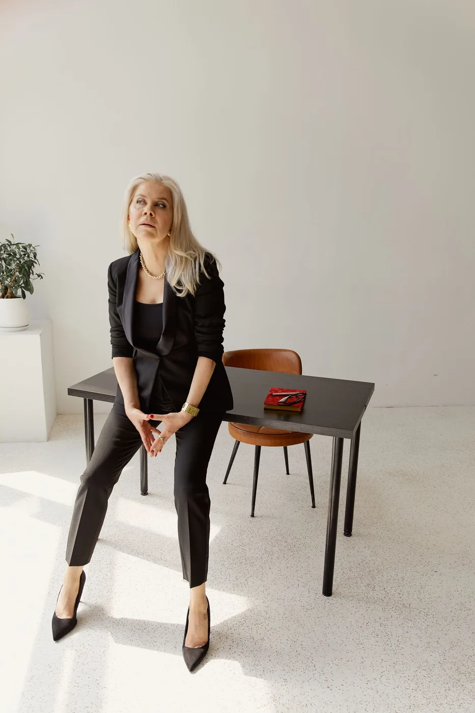 A woman in dark tailored separates seated beside a small table.
