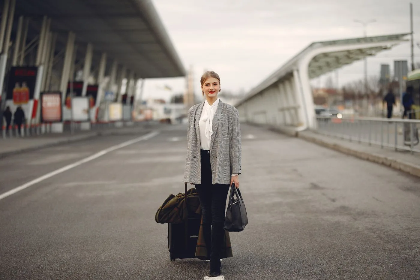 A woman wearing a pale outer layer and carrying a dark bag outside a terminal.