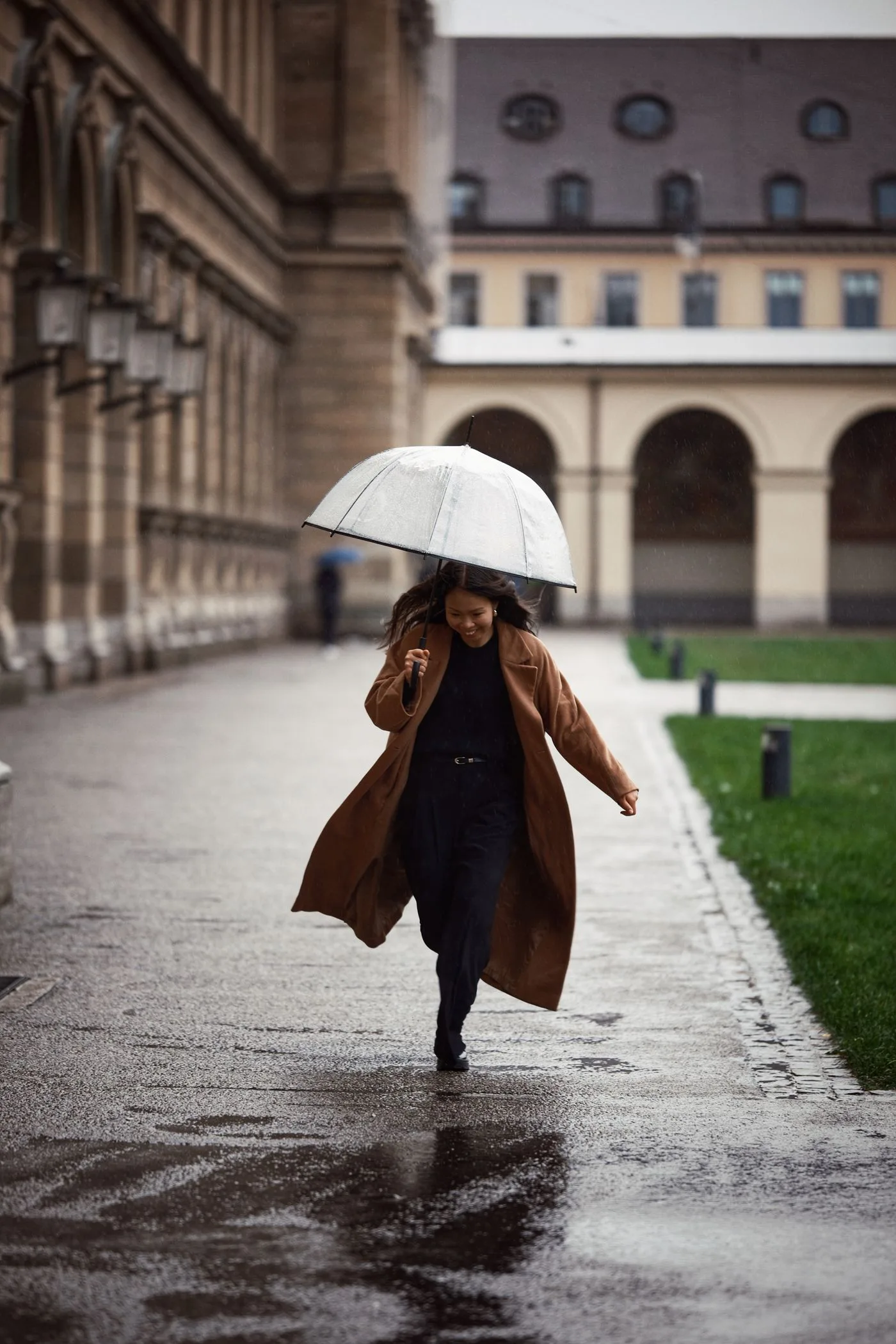 A woman in a brown coat carrying a pale umbrella on a city street.