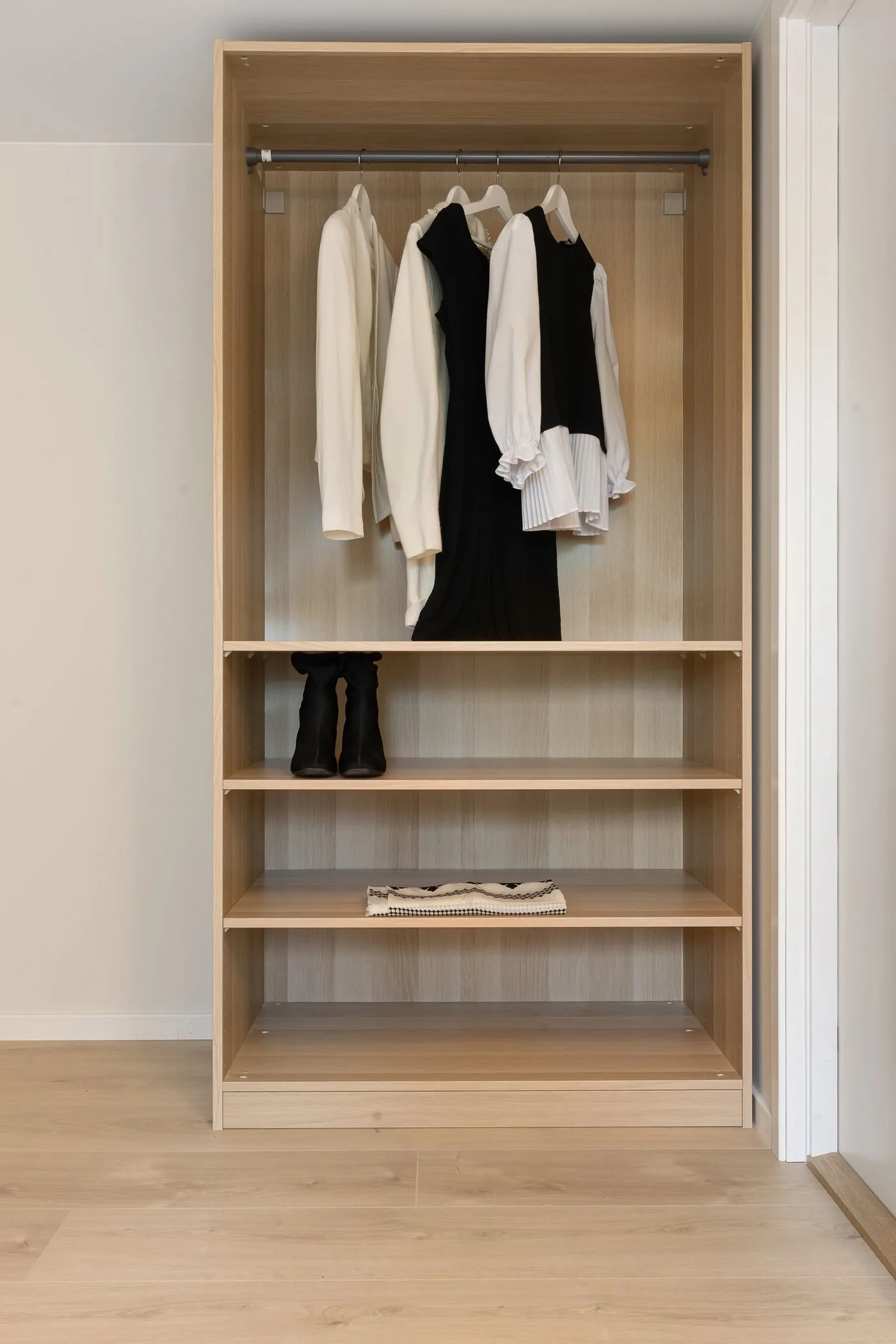 A wooden wardrobe with pale and dark hanging garments above open shelves.