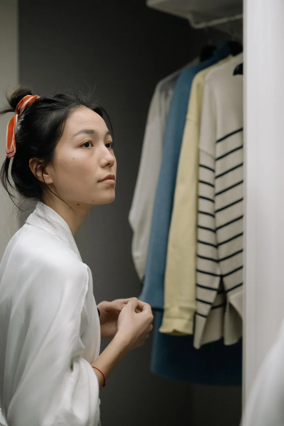 A woman beside hanging clothes in an open wardrobe.