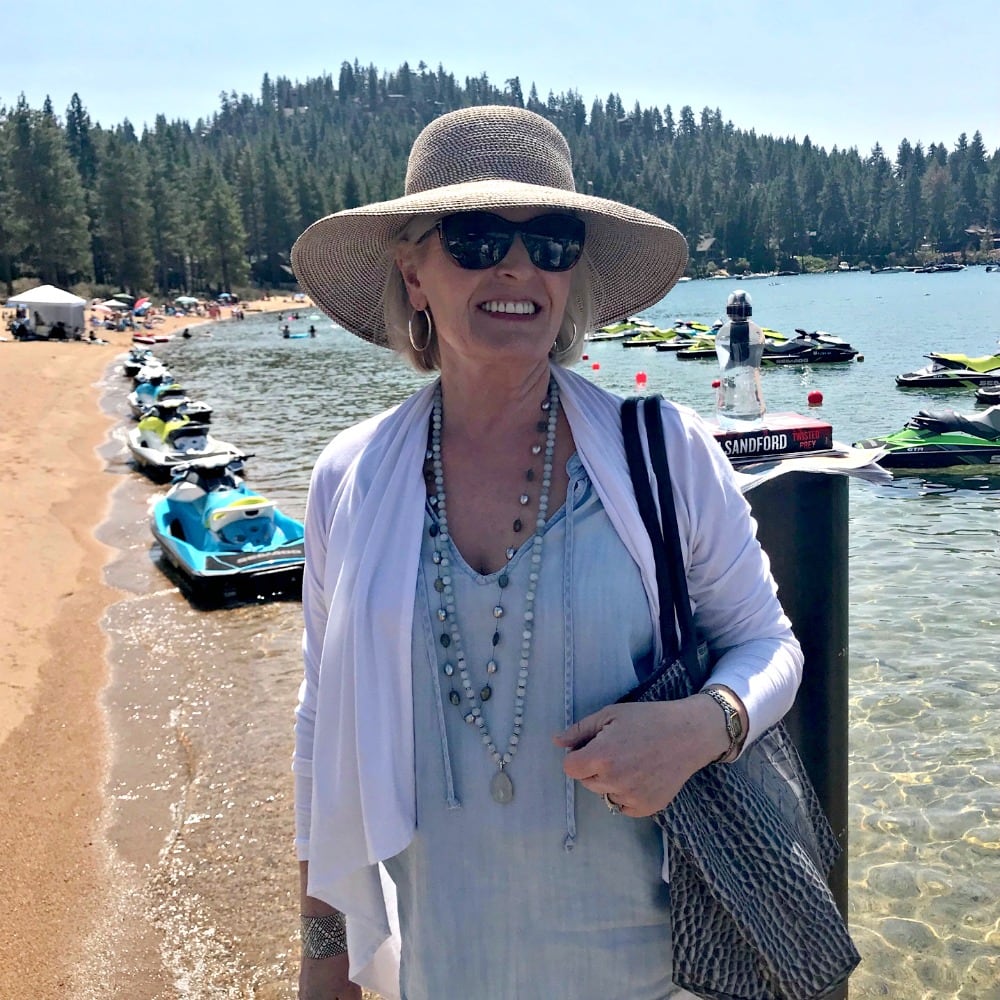 woman wearing Eric Javits hampton squishee packable hat with UPF50 on shaore of lake tahoe