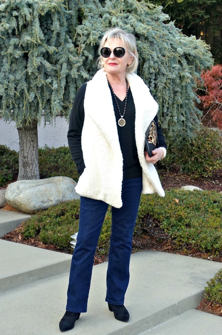 Jennifer Connolly wearing cream fuzzy vest over black v-neck, bootcut jeans and black booties