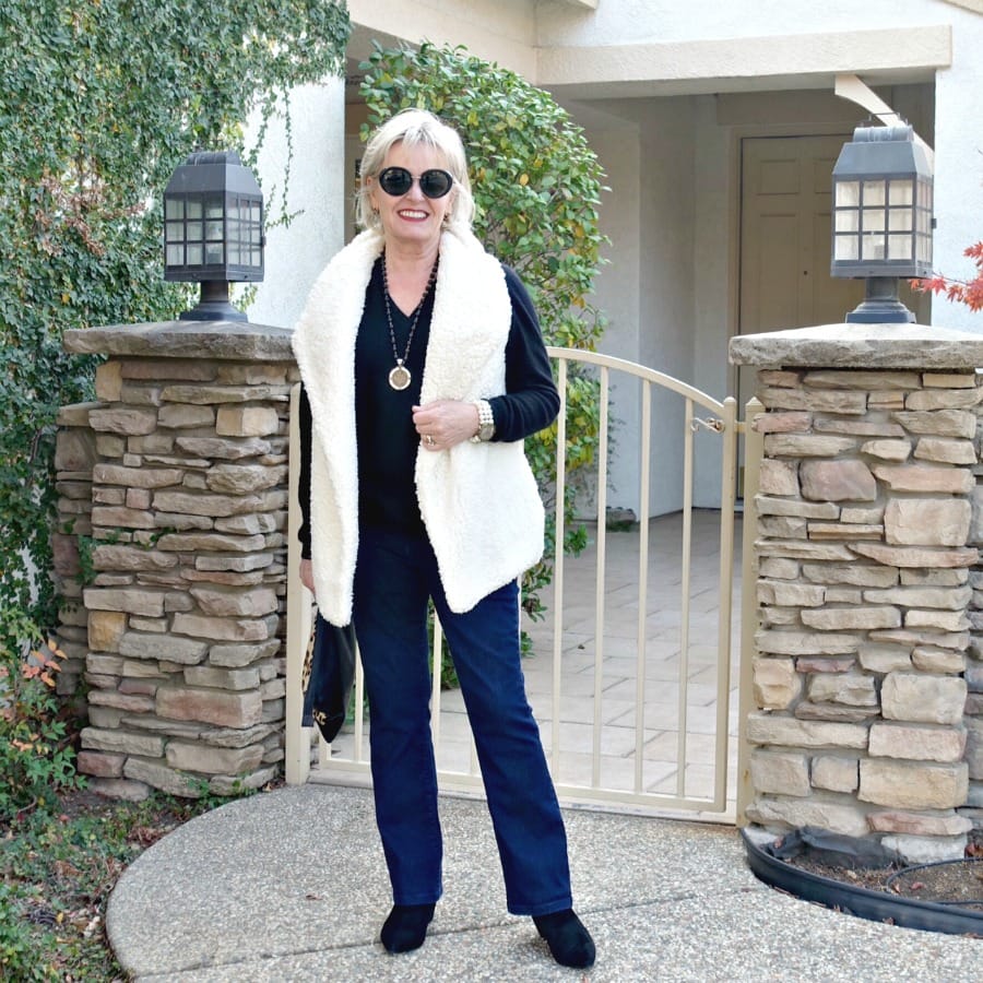 Jennifer Connolly of A Well Styled Life wearing fleece vest over black sweater with boot cut jeans