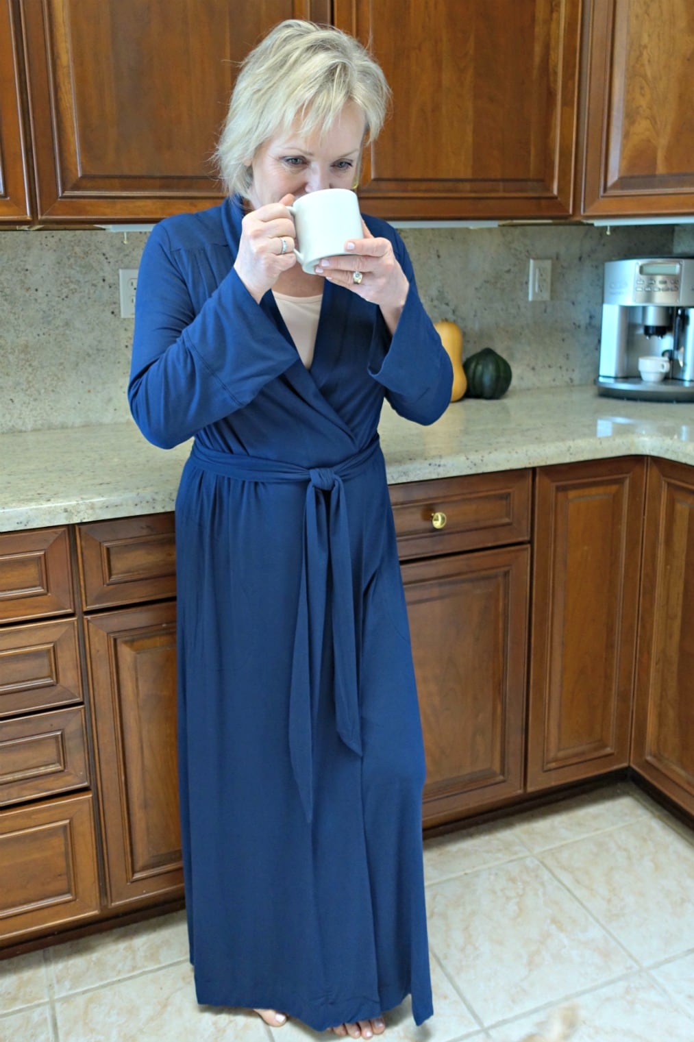 Jennifer of A Well Styled Life wearing Cool Nights Long Robe in Navy while drinking coffee in her kitchen