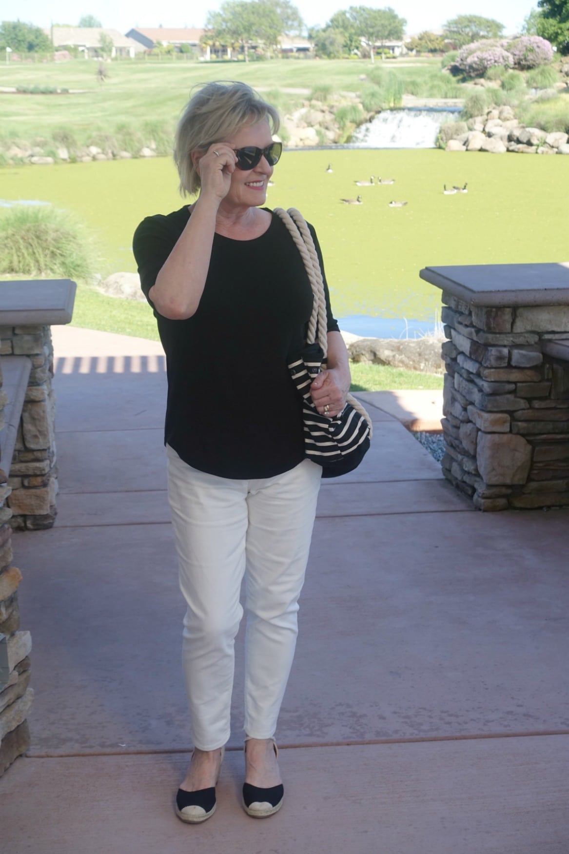 Jennifer of A Well Styled Life wearing black tee, cream colored jeans, black espadrilles and black striped tote