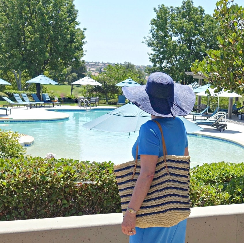 Over 50 style blogger Jennifer Connolly wearing a wide brimmed hat with UPF, a cotton dress and a a straw tote from Walmart