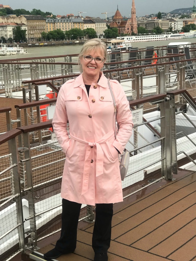 Jennifer Connolly of A Well Styled Life wearing Talbots pink trench coat on a Viking Cruise ship in Budapest pink trench from Talbot with black jeans on a Viking River boat in Bucarest