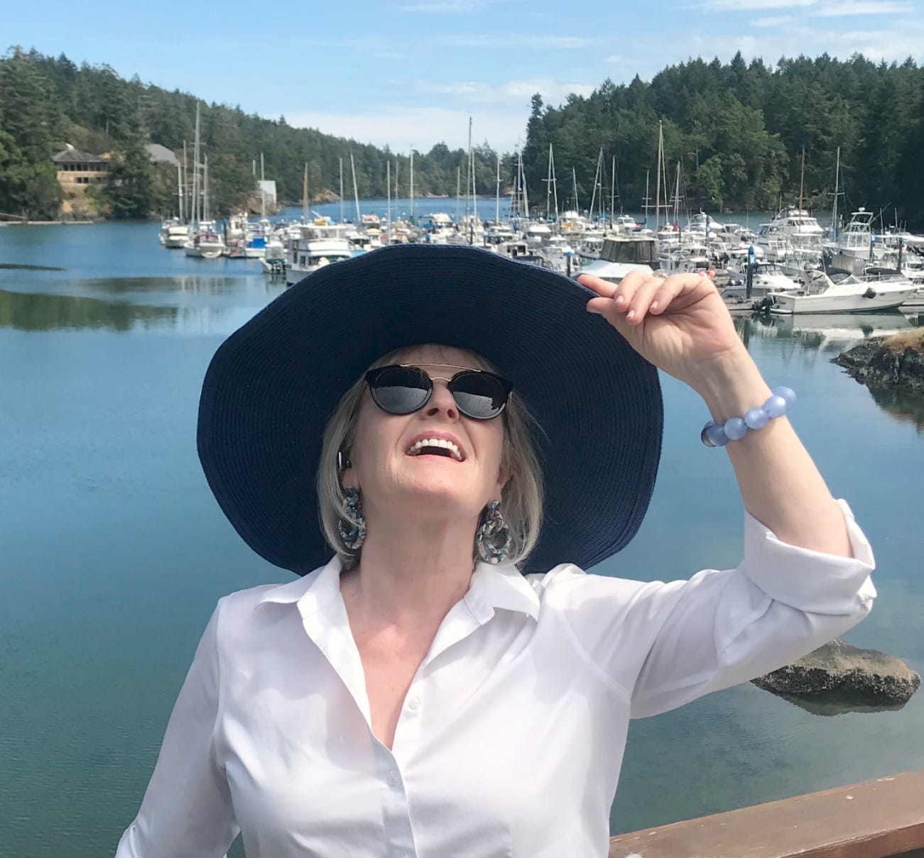Jennifer Connolly of A Well Styled Life wearing large blue hat and white shirt at a marina