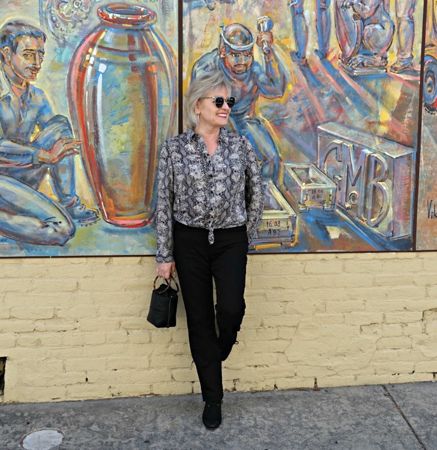 Jennifer Connolly of A Well Styled life wearing budget-friendly snakeskin spint blouse and black jeans standing against a wall mural