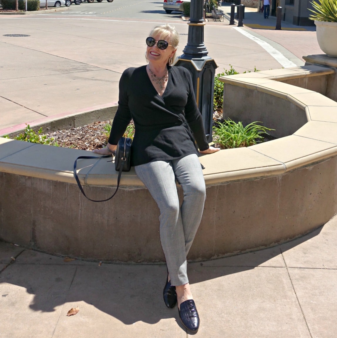 Jennifer Connolly of A Well Styled Life sitting on planter edge wearing the slim Essex pant from Talbots with black sweater