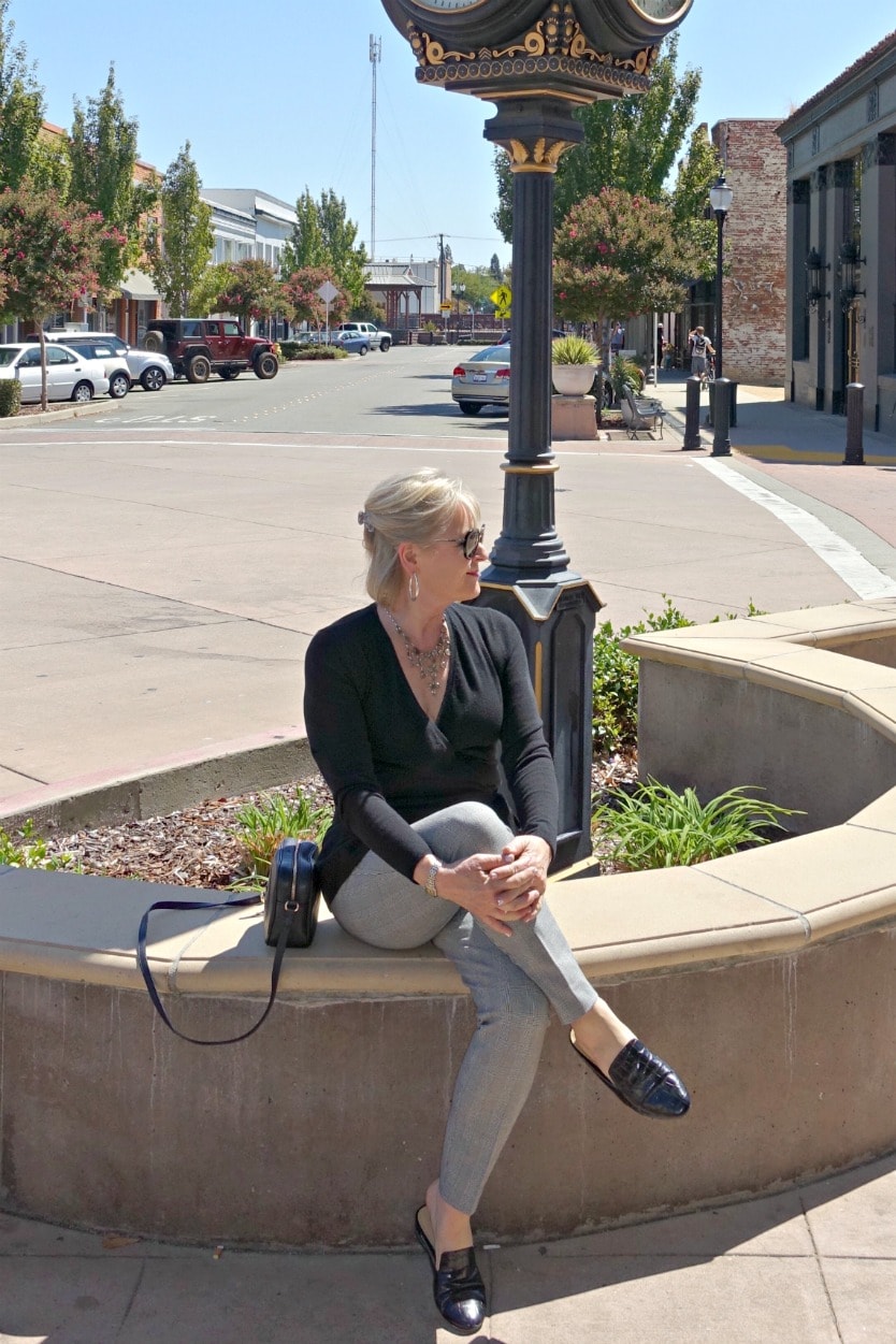 casual outfit of black sweater and plaid pants from Talbots on Jennifer Connolly sitting on a cement wall