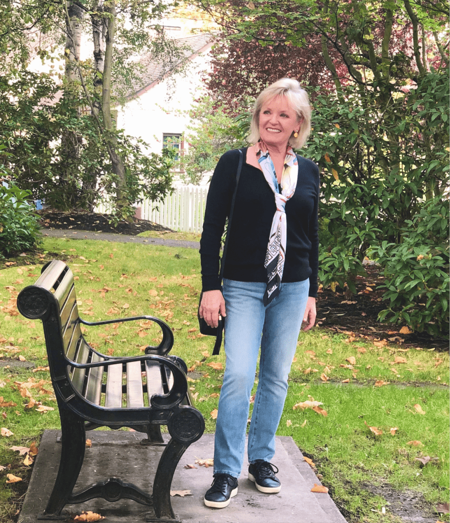 fashion blogger jennifer connolly wearing cashmere sweater and blue jeans in park near bench