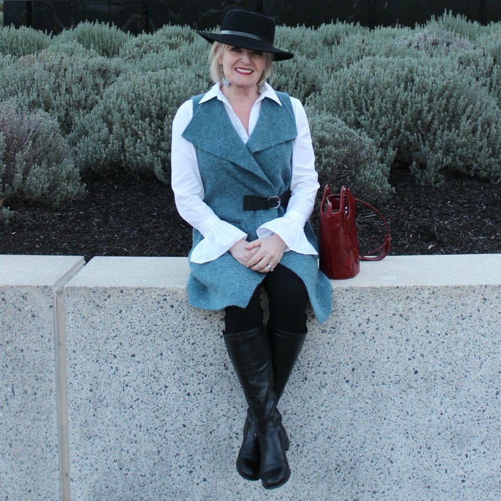 woman wearing black hat and teal sweater vest sitting on wall