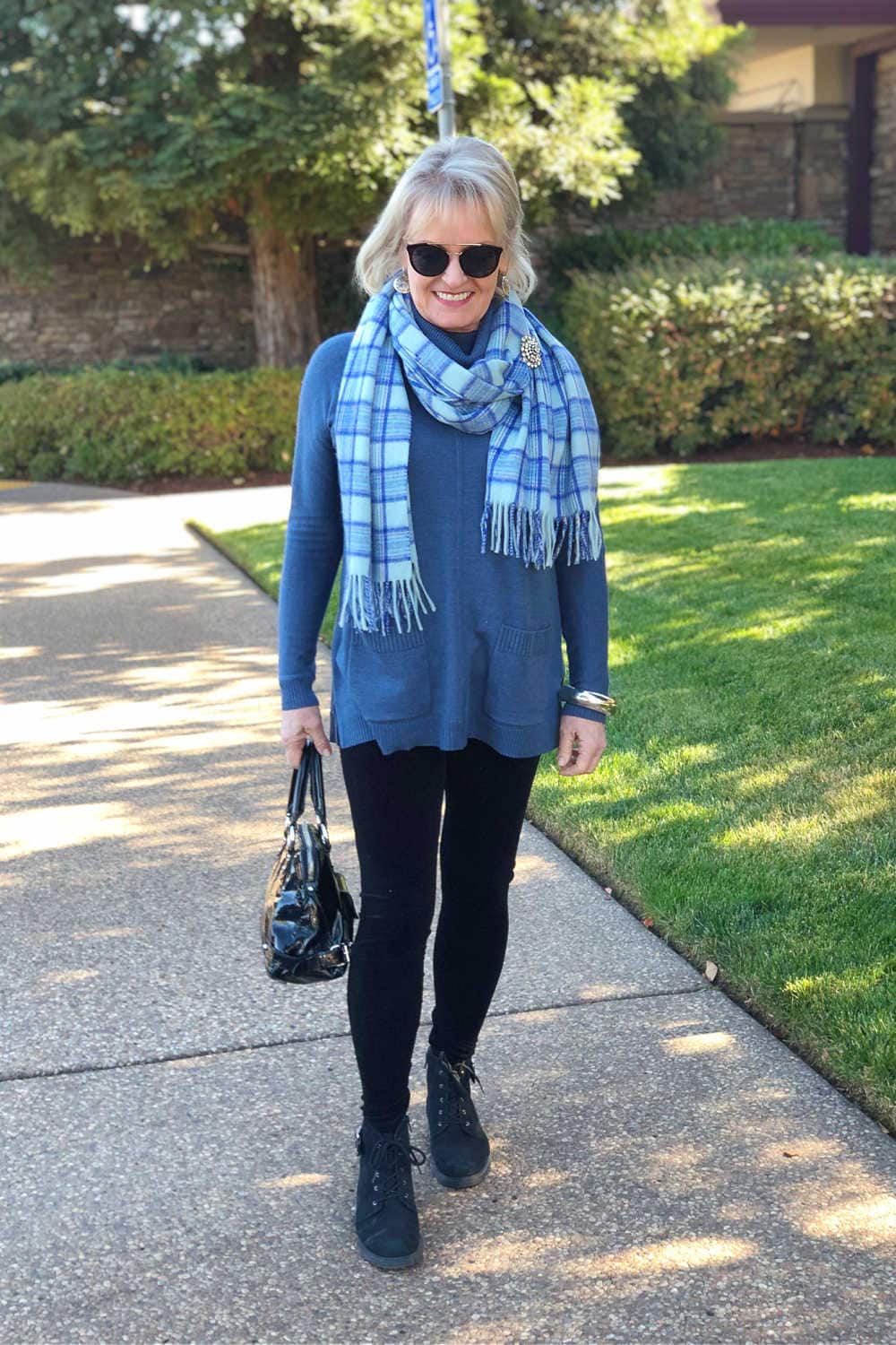 fashion blogger jennifer of a well styled life wearing velvet leggings, blue sweater tunic and plaid scarf walking on sidewalk