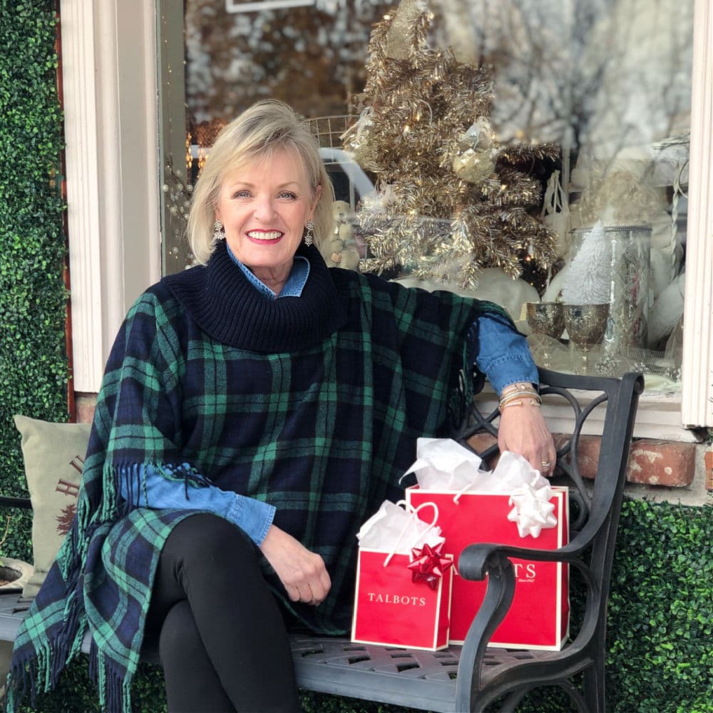 jennifer connolly of a well styled life sitting on bench with two red talbots bags wearing black watch plaid poncho