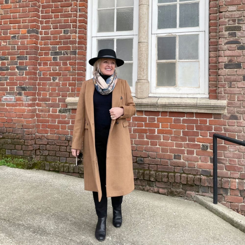 jennifer of a well styled life wearing camel coat, black jeans, navy turtleneck and black hat