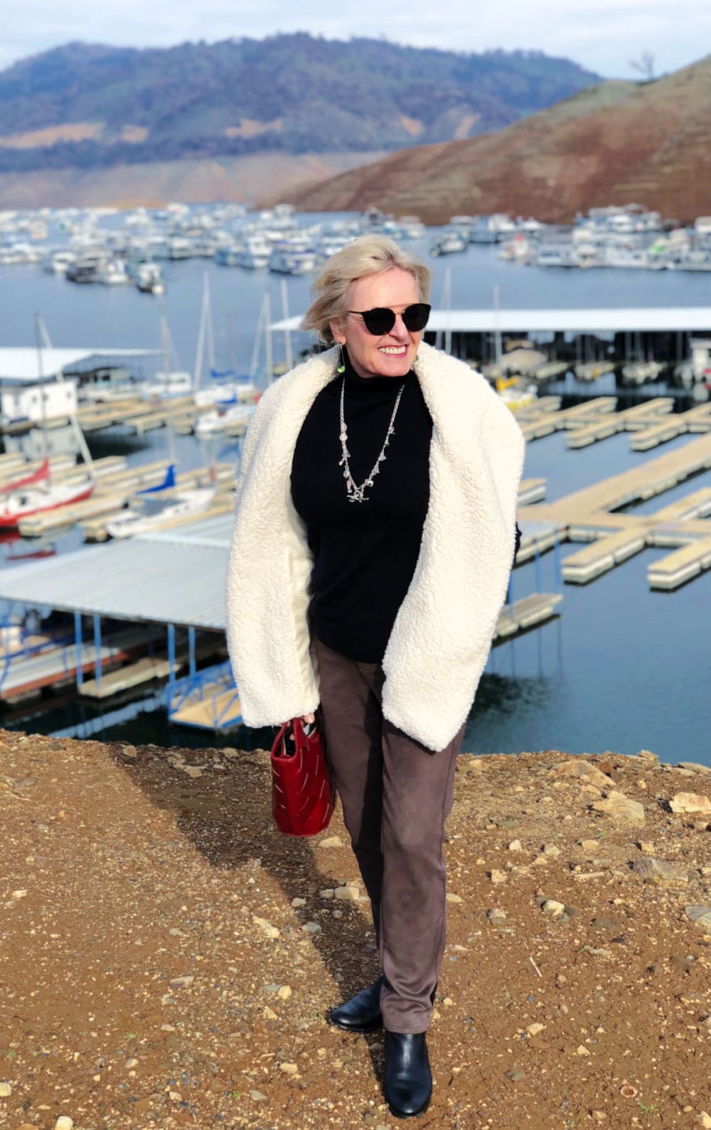 over 50 fashion blogger jennifer connolly of a well styled life wearing teddy bear vest and faux suede pants standing on bluff overlooking lake oroville